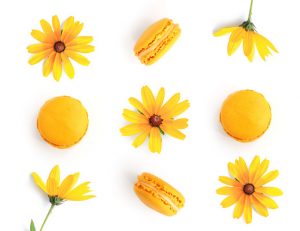 Creative layout made of yellow flowers and macaroons isolated on white background. Flat lay. Food concept.